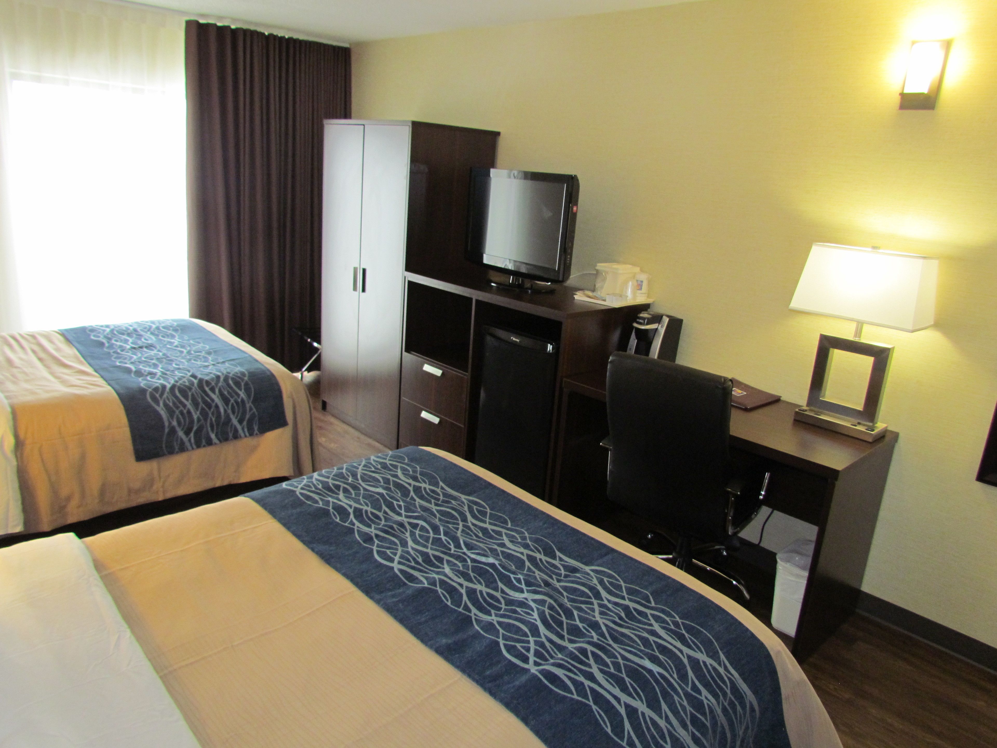 Una habitación de hotel con dos camas, un escritorio con ordenador, televisor y lámpara.