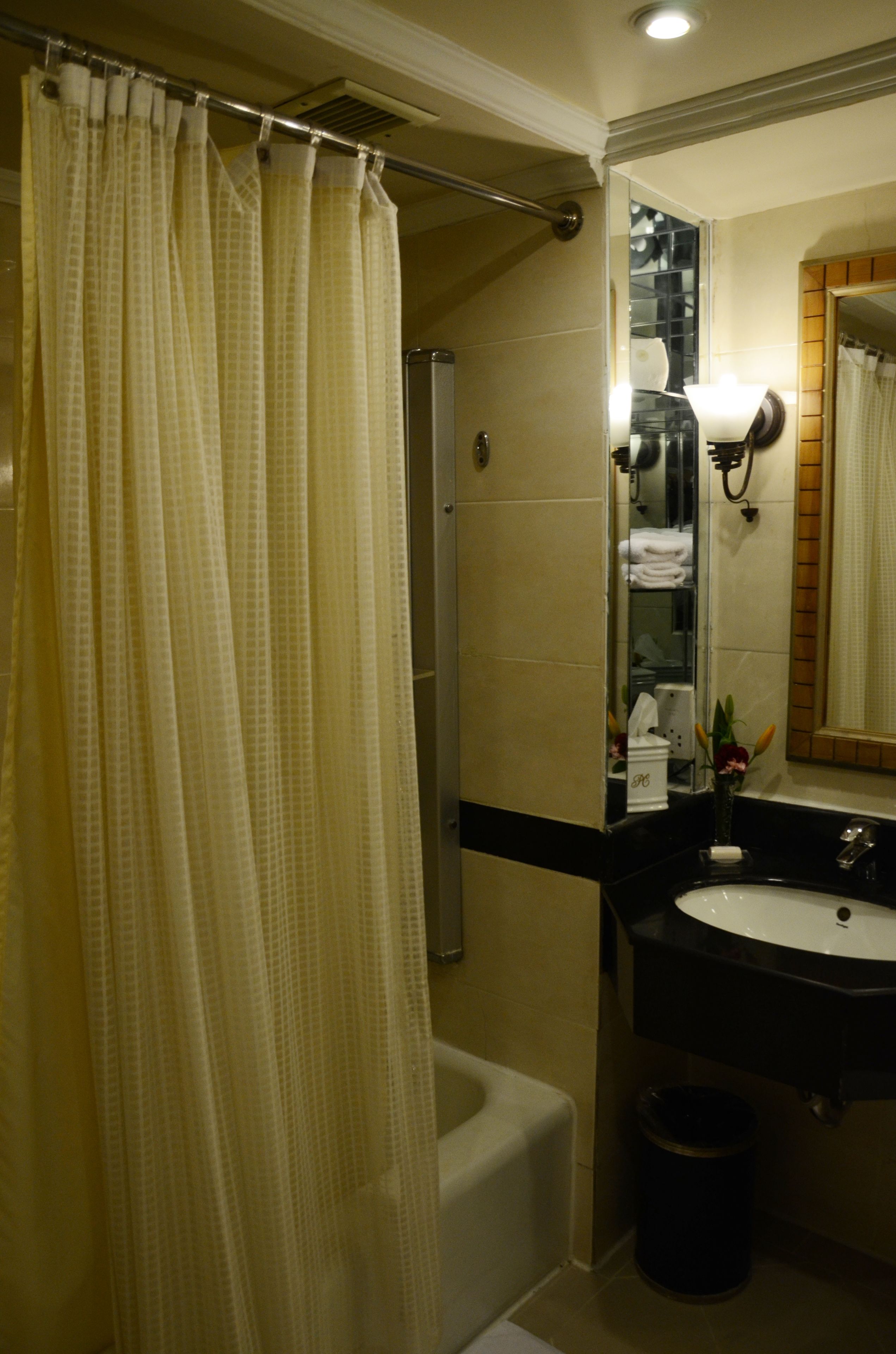 A bathroom with a shower, a sink, a mirror, and a trash can.