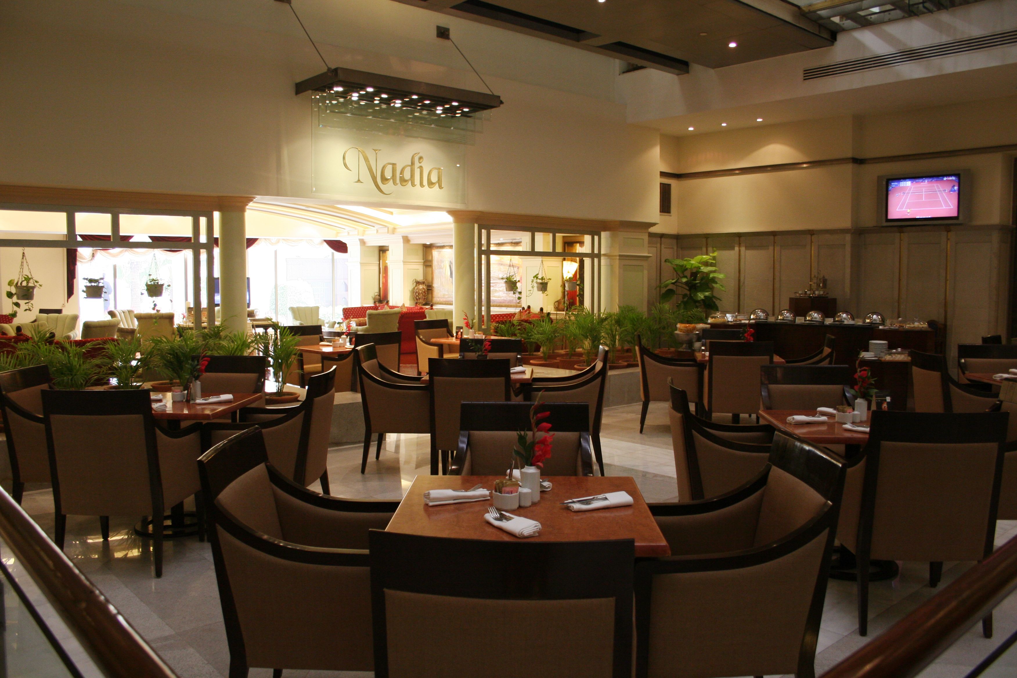 A restaurant with multiple dining tables and chairs, a TV screen, and potted plants.