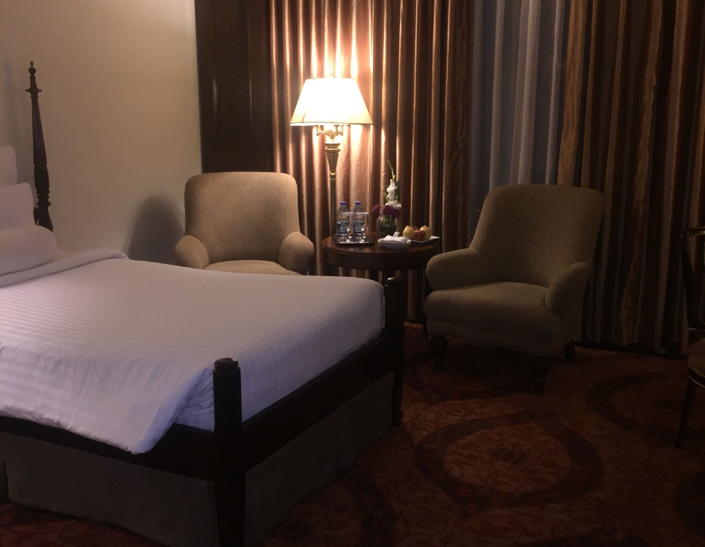 Ein Hotelzimmer mit einem Bett, zwei Sesseln, einem Tisch mit einer Lampe und einem Vorhang im Hintergrund.