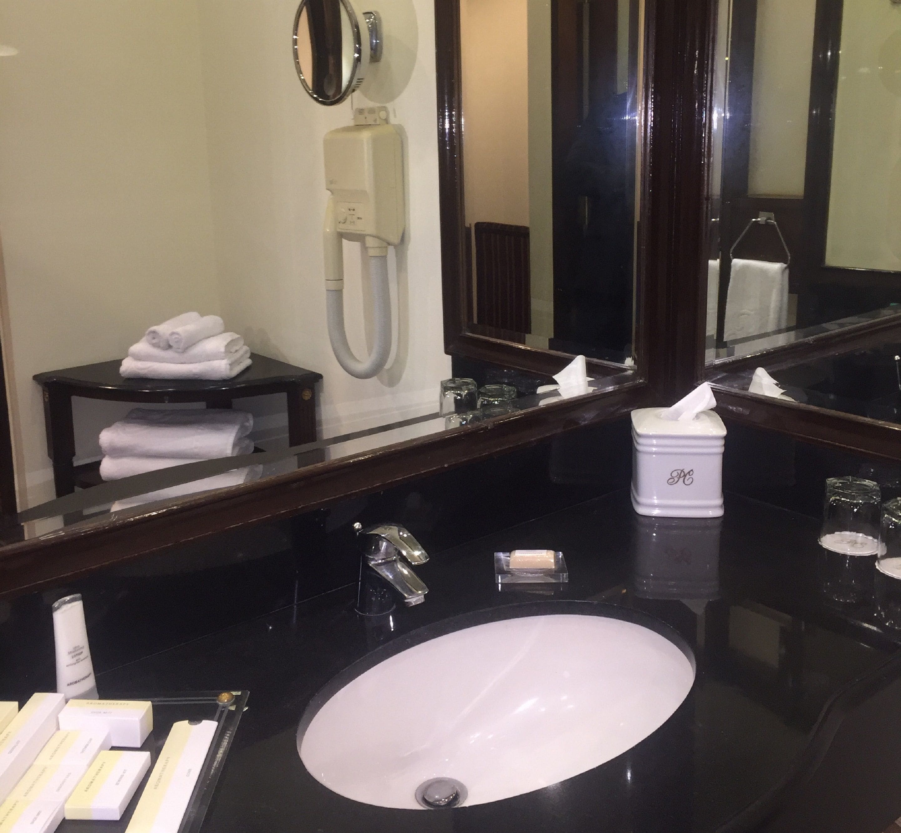 A hotel bathroom with a large mirror, a sink, a towel rack, and a tissue dispenser.