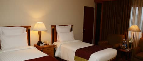 Habitación de hotel con dos camas, un escritorio, una silla y una lámpara.