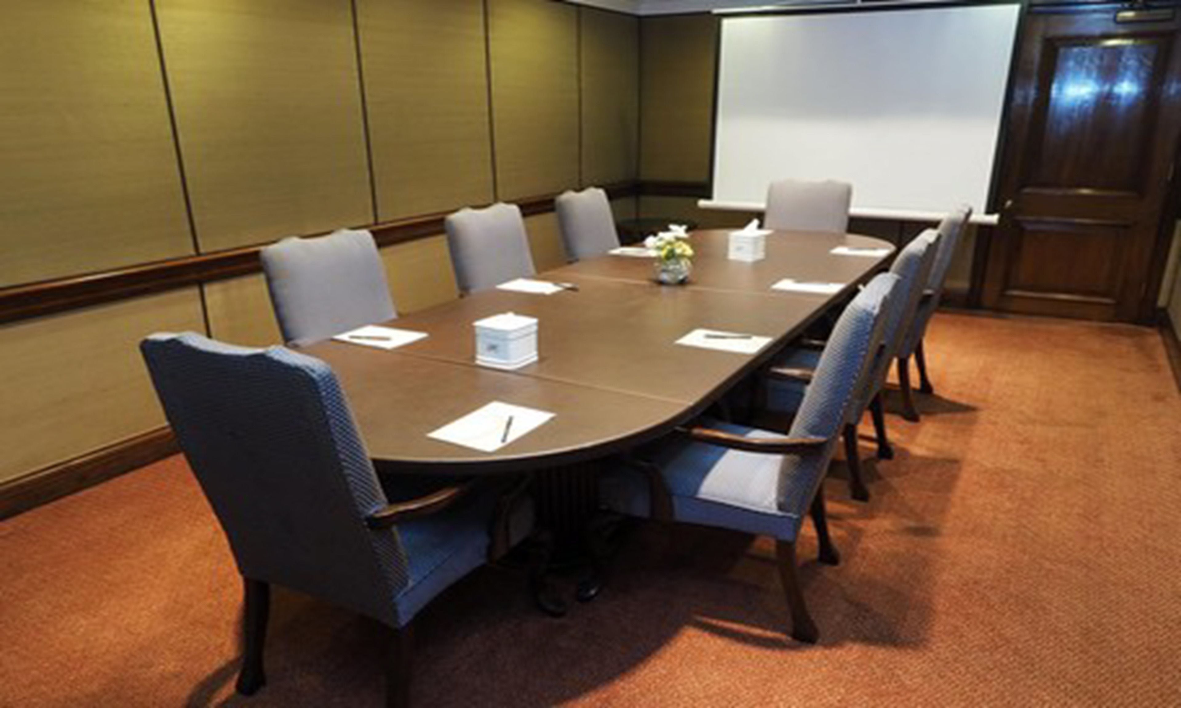 Un salón de conferencias con una larga mesa, seis sillas y una pantalla de proyector.