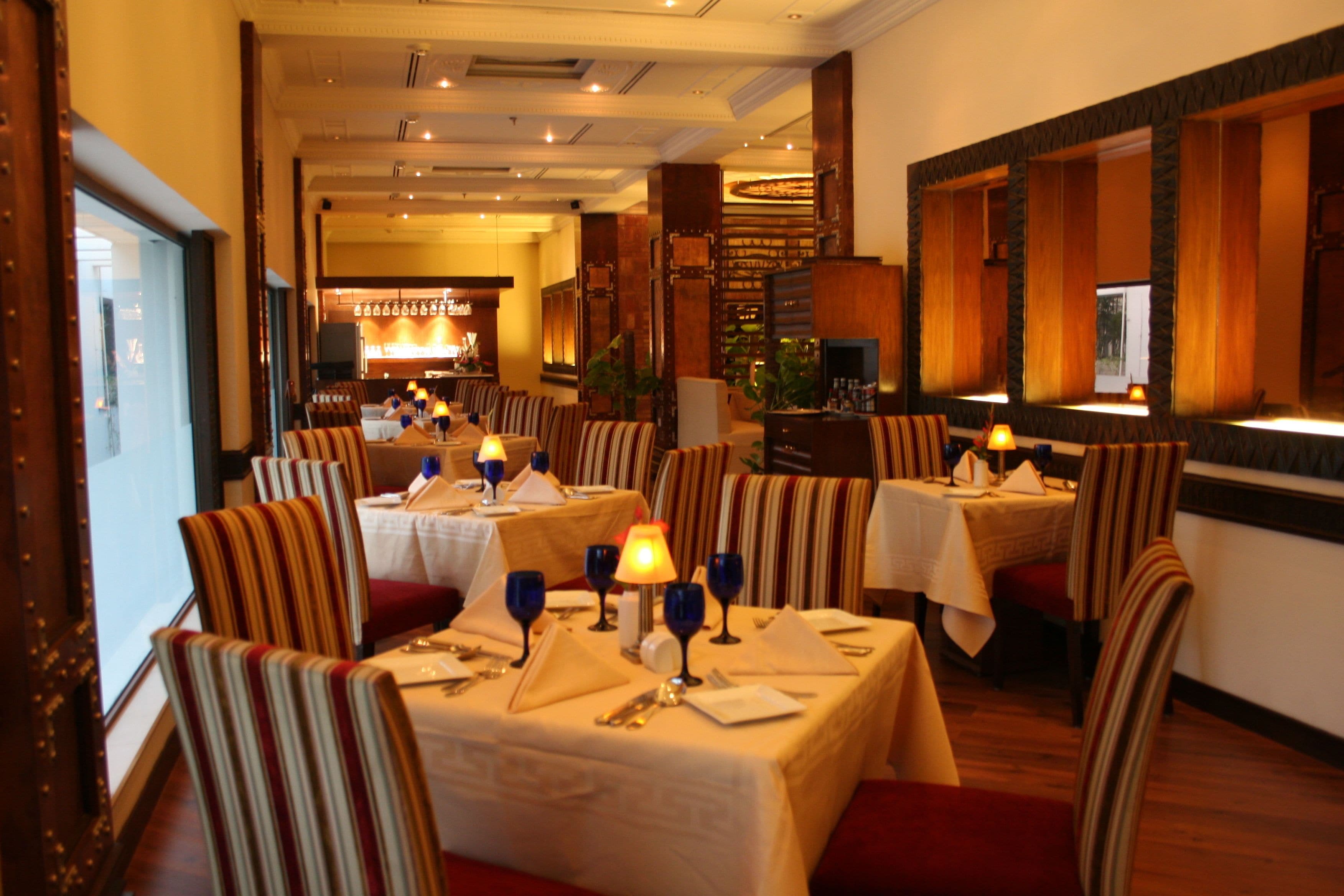 Ein Restaurant mit mehreren Tischen, gestreiften Stühlen und warmer Beleuchtung.