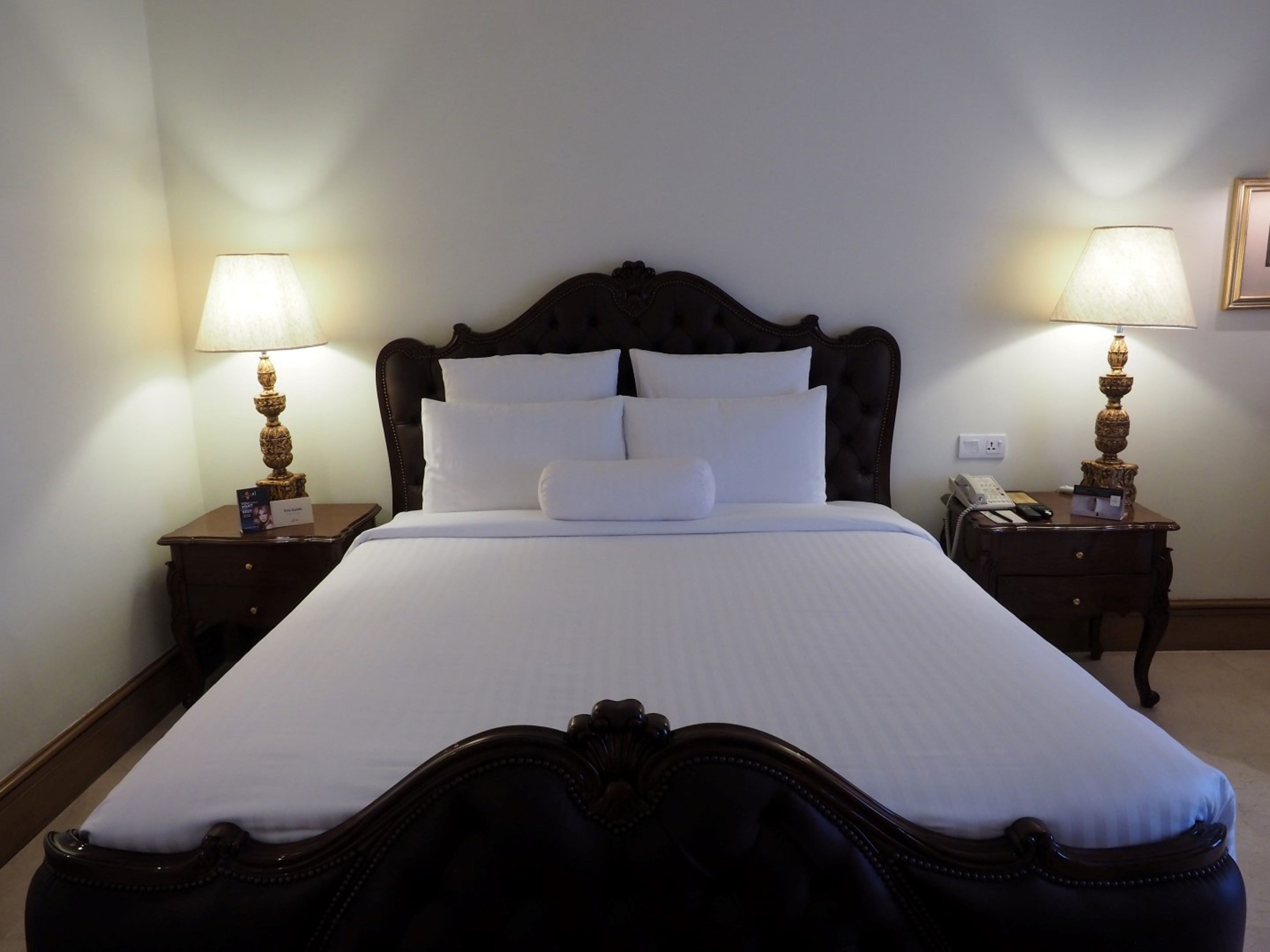 A neatly made bed with white linens, two bedside tables with lamps, and a framed picture on the wall.