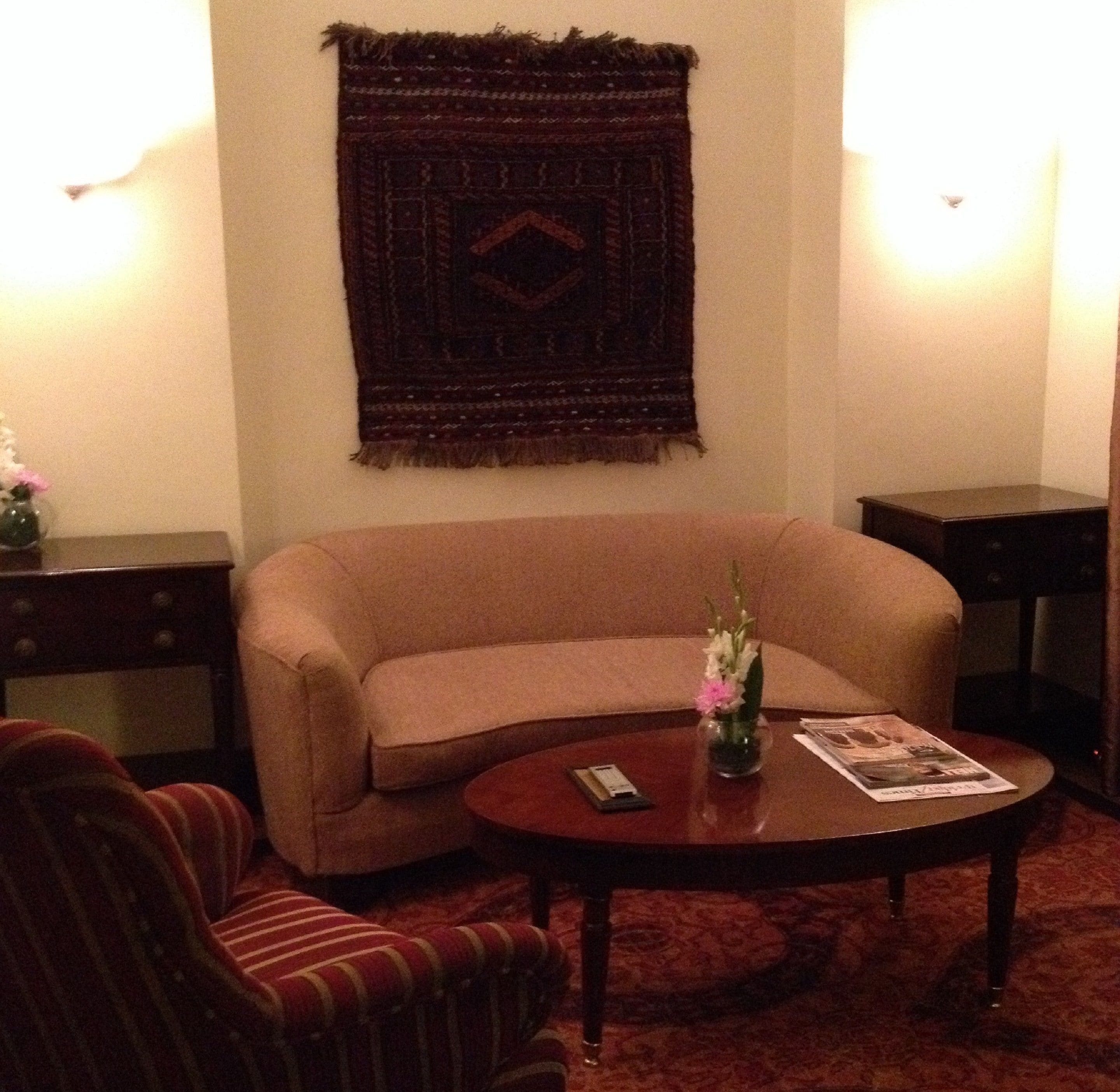 A living room with a sofa, a striped armchair, a coffee table, a vase with flowers, and a magazine.