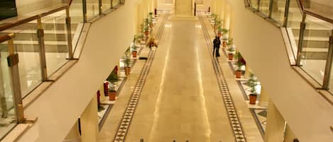 Ein geräumiges Atrium mit einer zentralen Rolltreppe, gesäumt von Glasgeländern und Topfpflanzen.