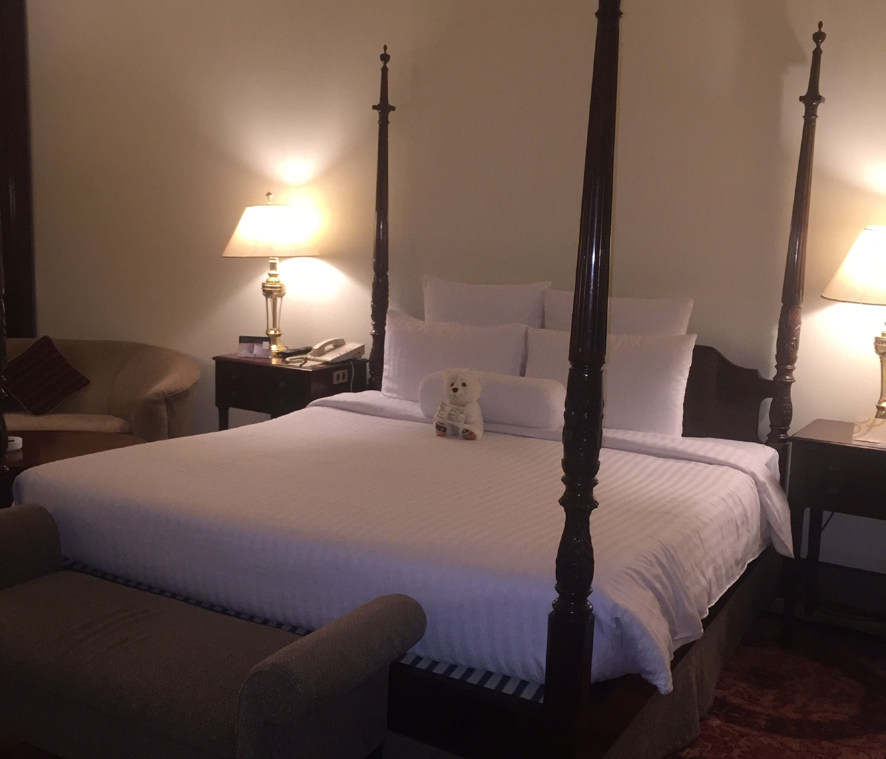 Una cama con dosel con sábanas blancas, una mesita de noche con lámpara y una silla.
