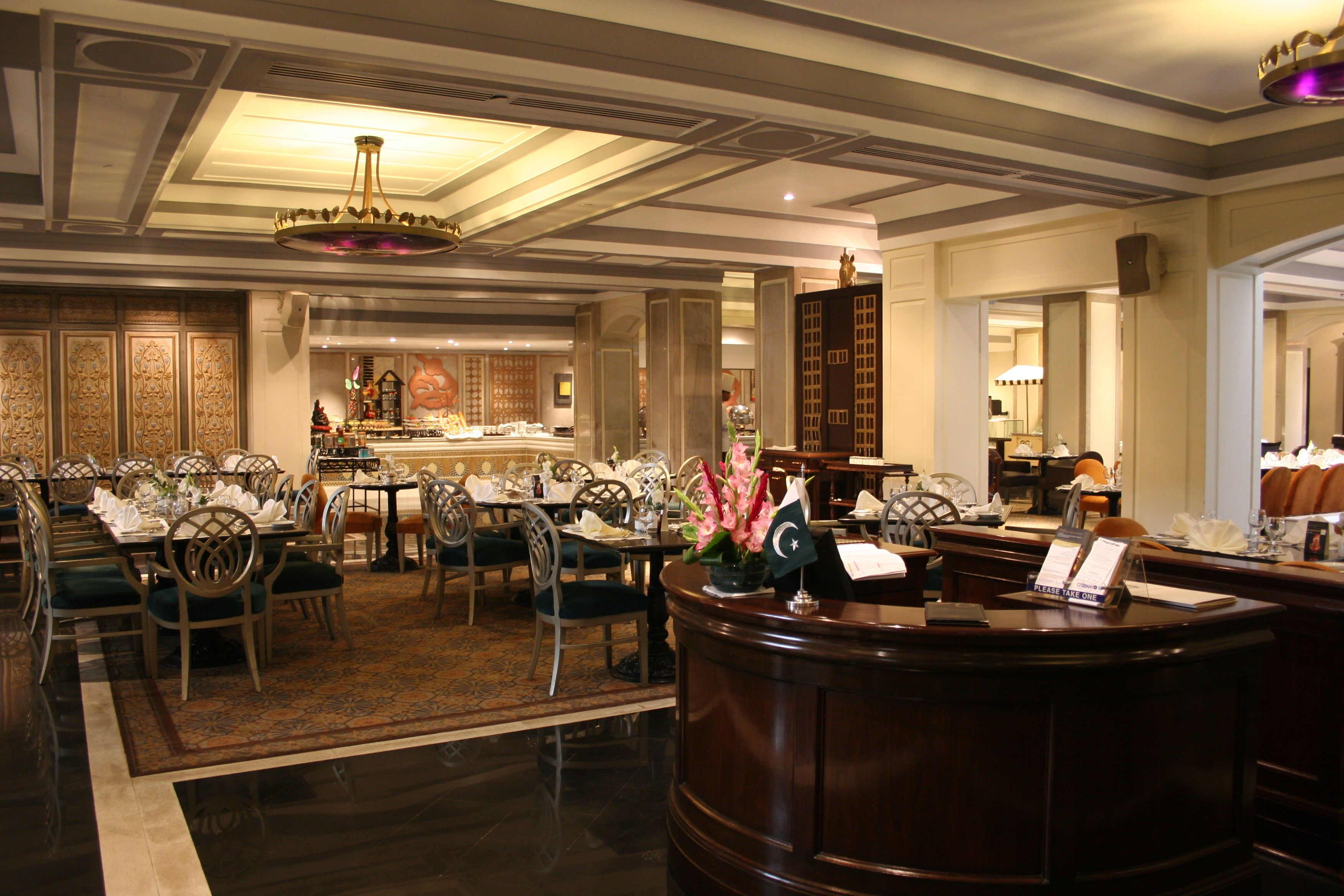 A hotel lobby with a reception desk, dining area, and a chandelier.