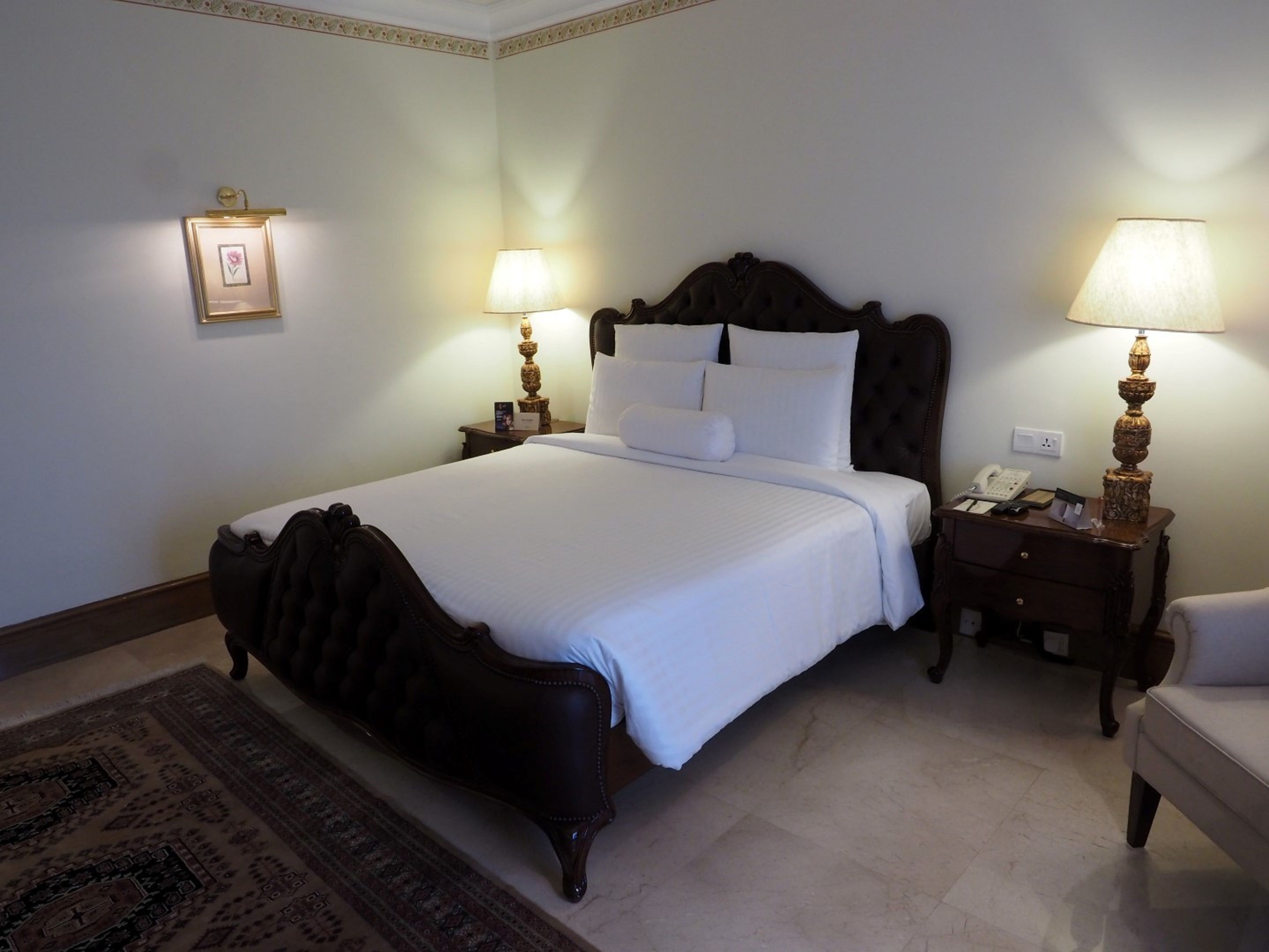 A neatly made bed with white linens, two bedside lamps, a small bedside table with a phone, and a framed picture on the wall.
