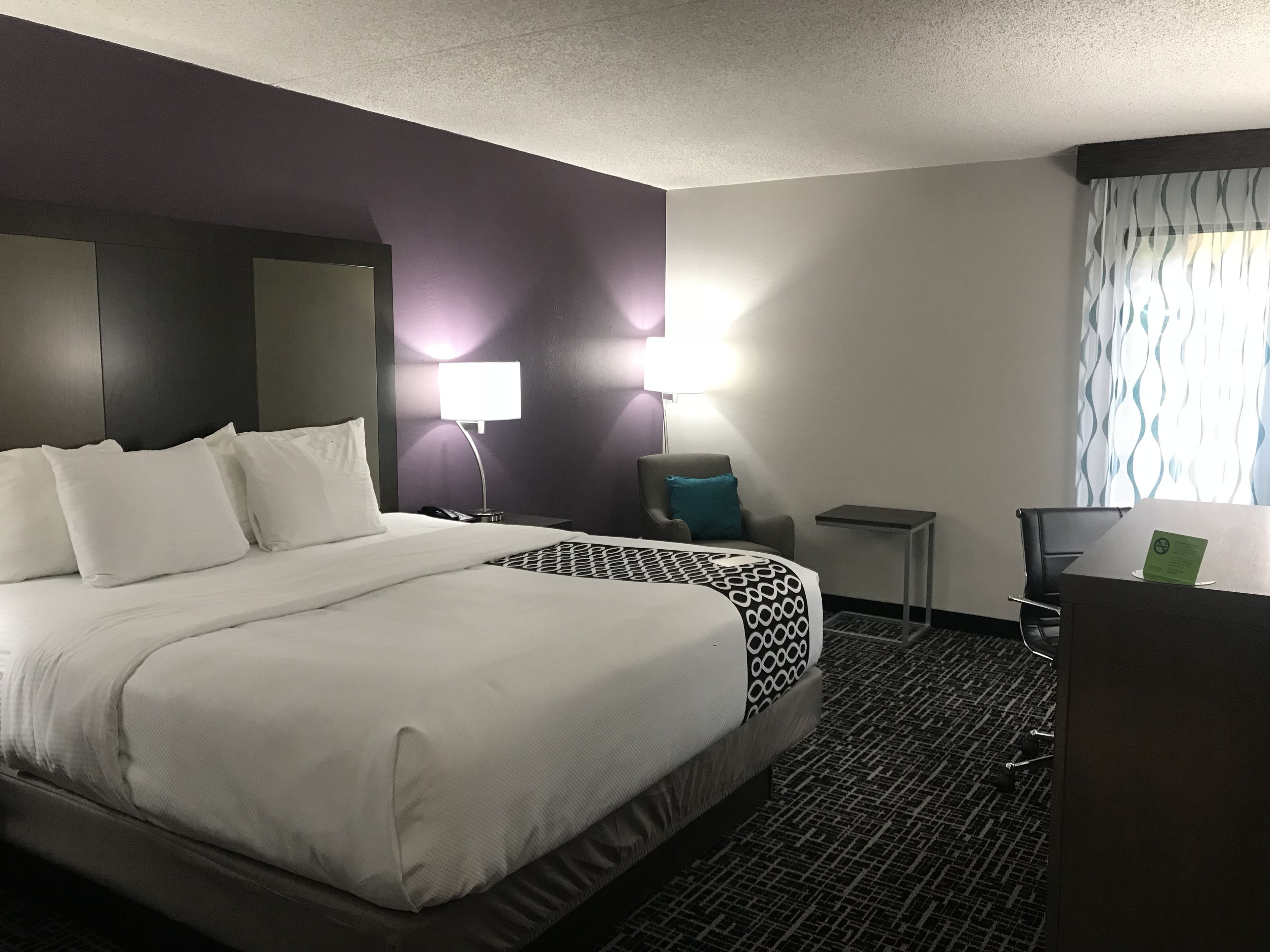 A hotel room with a large bed, a desk, a chair, a lamp, and a window with curtains.