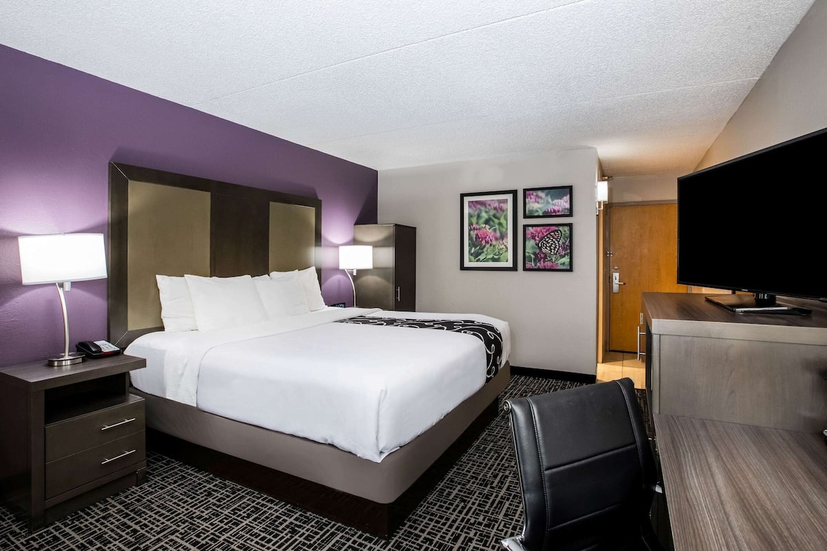 A hotel room with a bed, bedside tables, a desk, a chair, and a television.