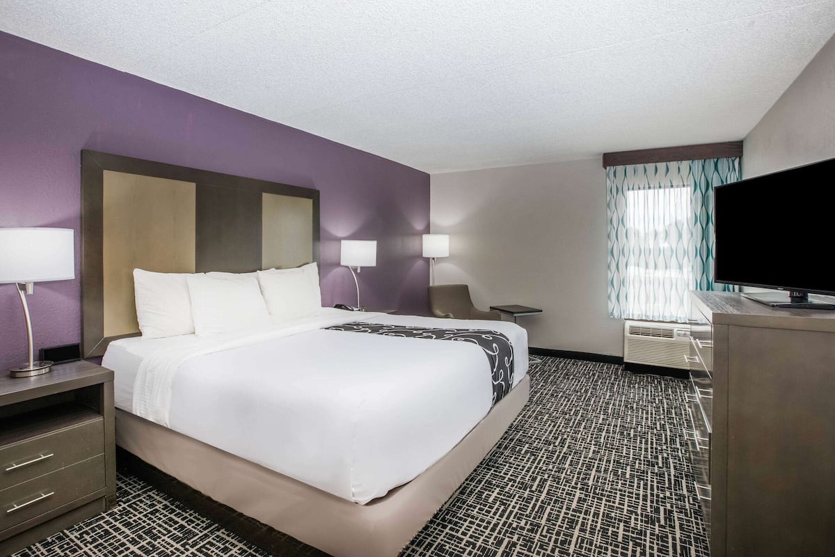A hotel room with a large bed, two bedside lamps, a flat-screen TV, a desk, and a window with curtains.