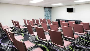 Un salón de conferencias con filas de sillas, un televisor de pantalla plana en la pared y una alfombra estampada.