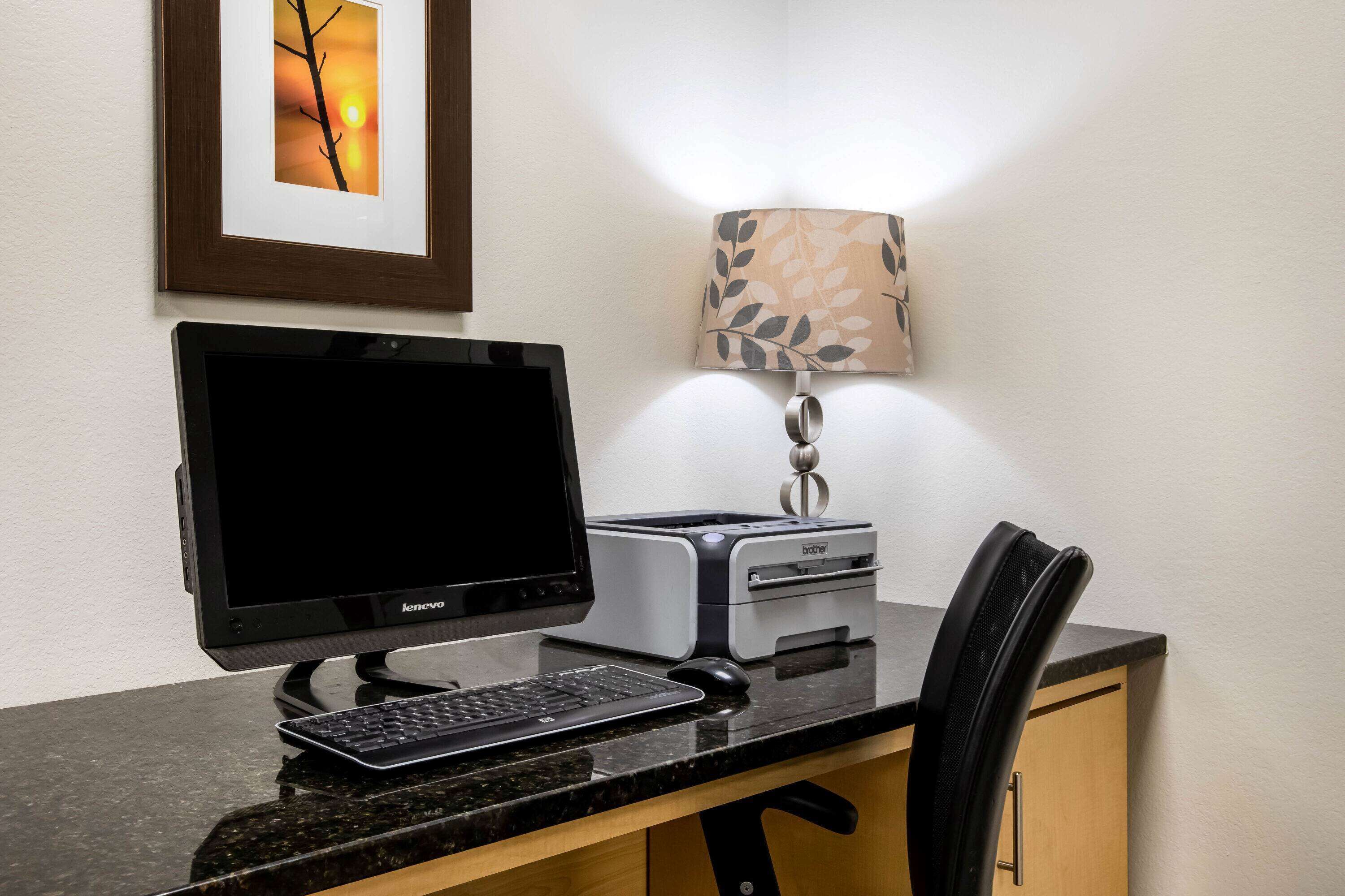Ein Schreibtisch mit einem Lenovo-Monitor, einer Tastatur, einem Drucker und einem Stuhl.