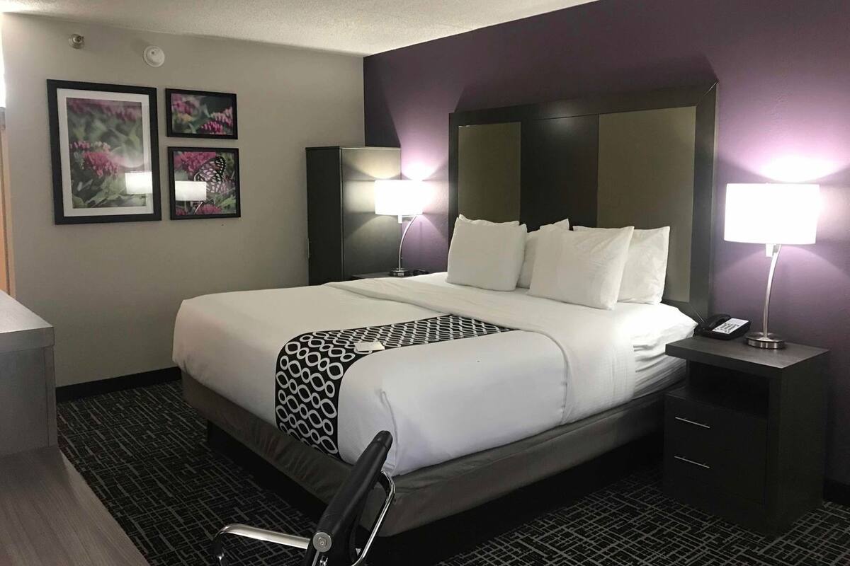 A hotel room with a large bed, two bedside lamps, a nightstand with a phone, and two framed pictures on the wall.