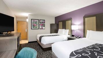 A hotel room with two beds, a desk with a flat-screen TV, a chair, and a carpeted floor.