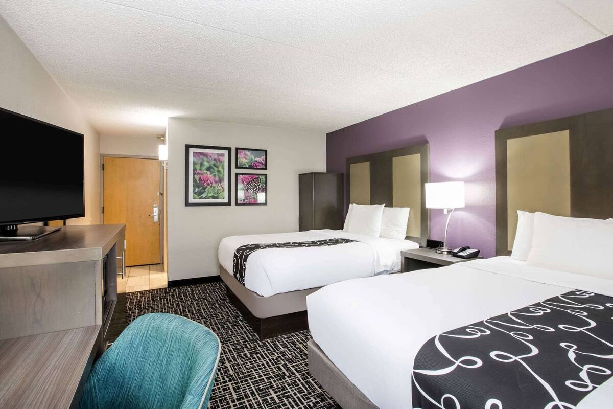 A hotel room with two beds, a desk with a TV, a chair, and a door leading to a bathroom.