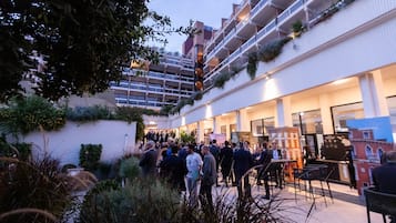 Ein heller Innenhof mit vielen Menschen, einem Café-Bereich und Blick auf ein Gebäude mit Balkonen.