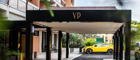 A covered entrance to a building with a 'VP' sign, a yellow car parked inside, and a bike in the background.