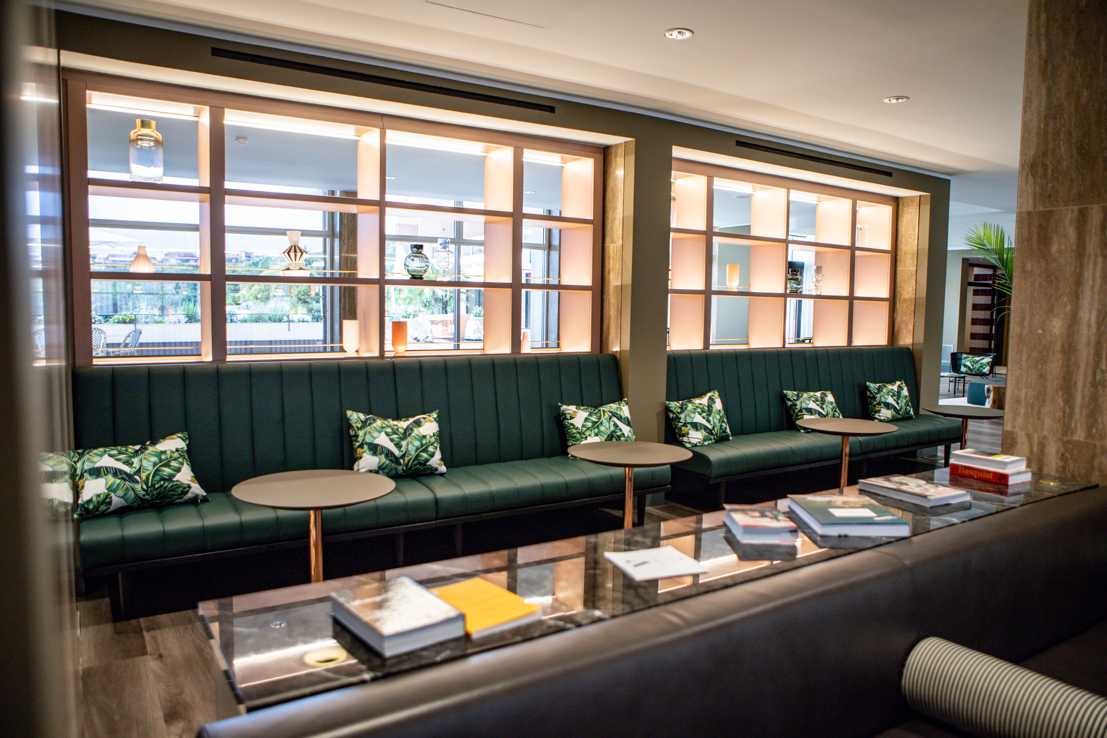 A modern lounge area with green sofas, round tables, and a glass coffee table.