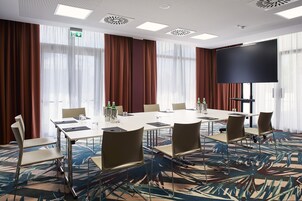 A conference room with a large table, chairs, a flat-screen TV, and a patterned carpet.