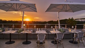 Ein Restaurant mit Tischen, Stühlen und Sonnenschirmen auf dem Dach, mit Blick auf einen malerischen Sonnenuntergang.
