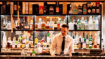 Un espace bar avec des étagères remplies de différentes bouteilles d’alcool, un barman derrière le comptoir et un intérieur bien éclairé.