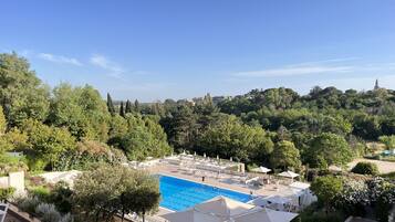 A pool area with lounge chairs and umbrellas, surrounded by lush greenery and trees.