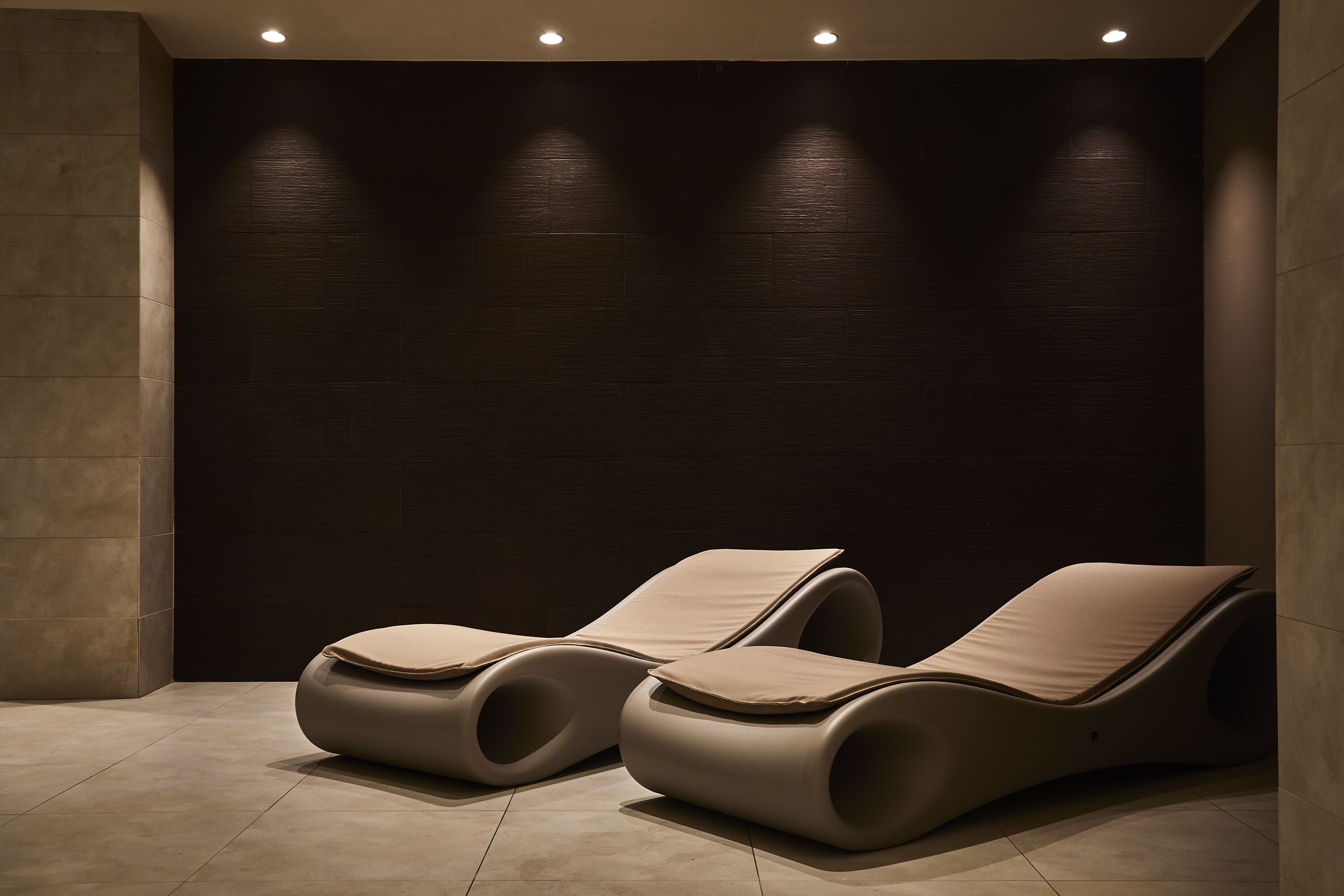 Un espacio moderno de relajación con dos sillones reclinables y una pared oscura.