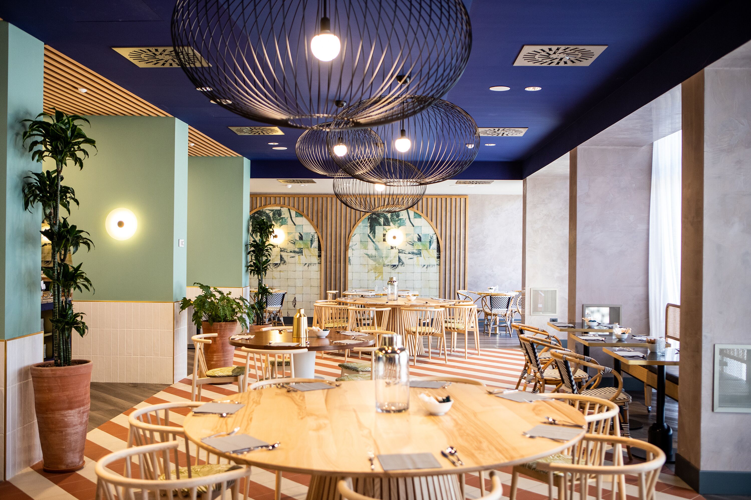 A spacious conference room with round tables, wooden chairs, and potted plants.