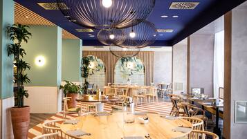 A spacious conference room with round tables, wooden chairs, and potted plants.