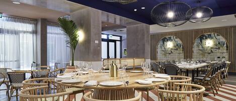 A spacious dining area with round tables and wicker chairs, featuring a modern ceiling design and large windows.