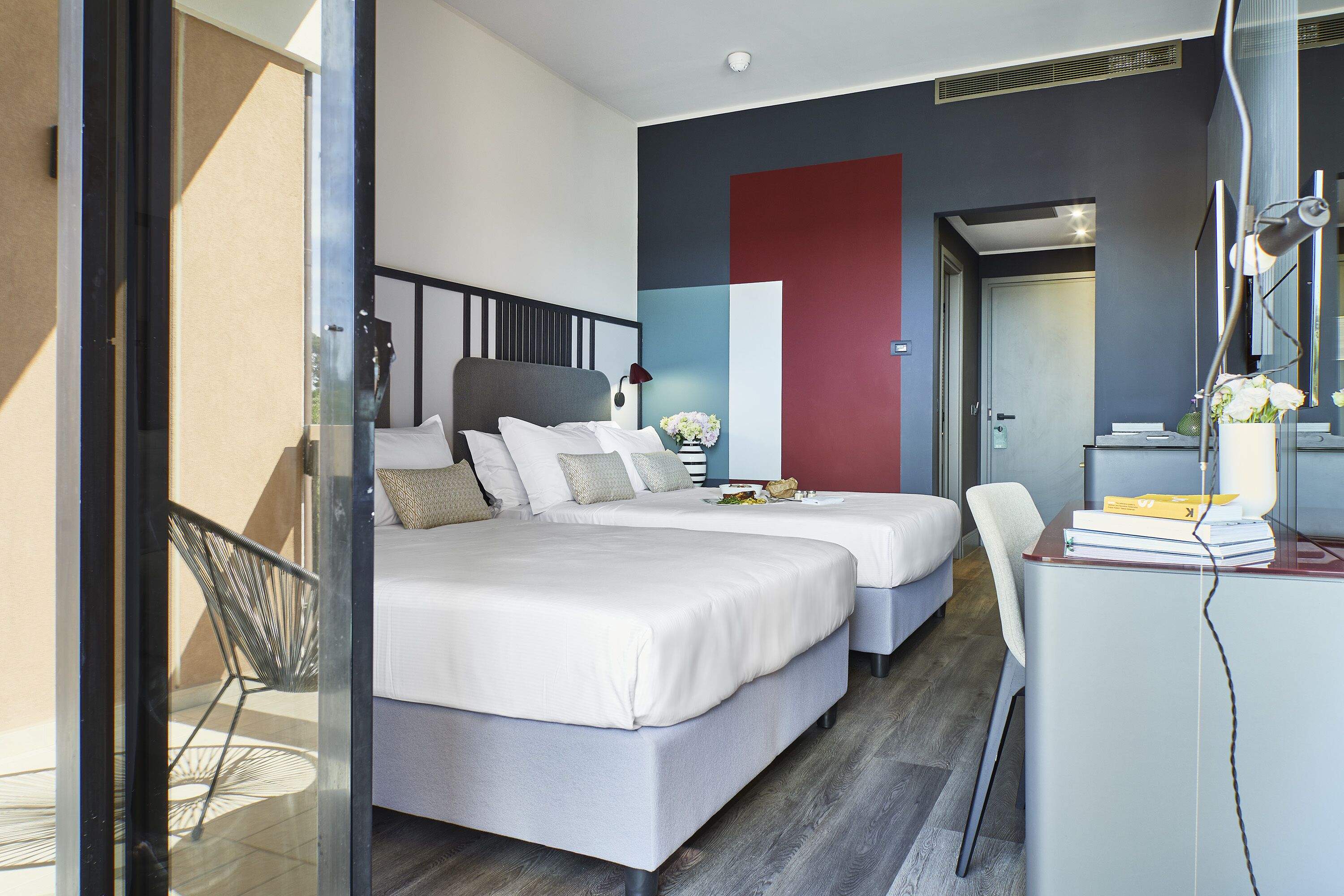 A modern hotel room with two beds, a desk with a chair, and a view of the outdoors.