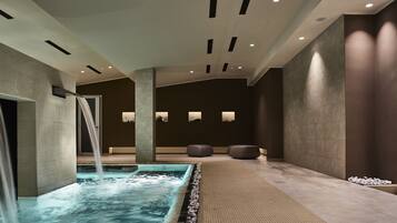Un espace piscine intérieur moderne, agrémenté d’une cascade, d’un éclairage encastré et de coins salon.