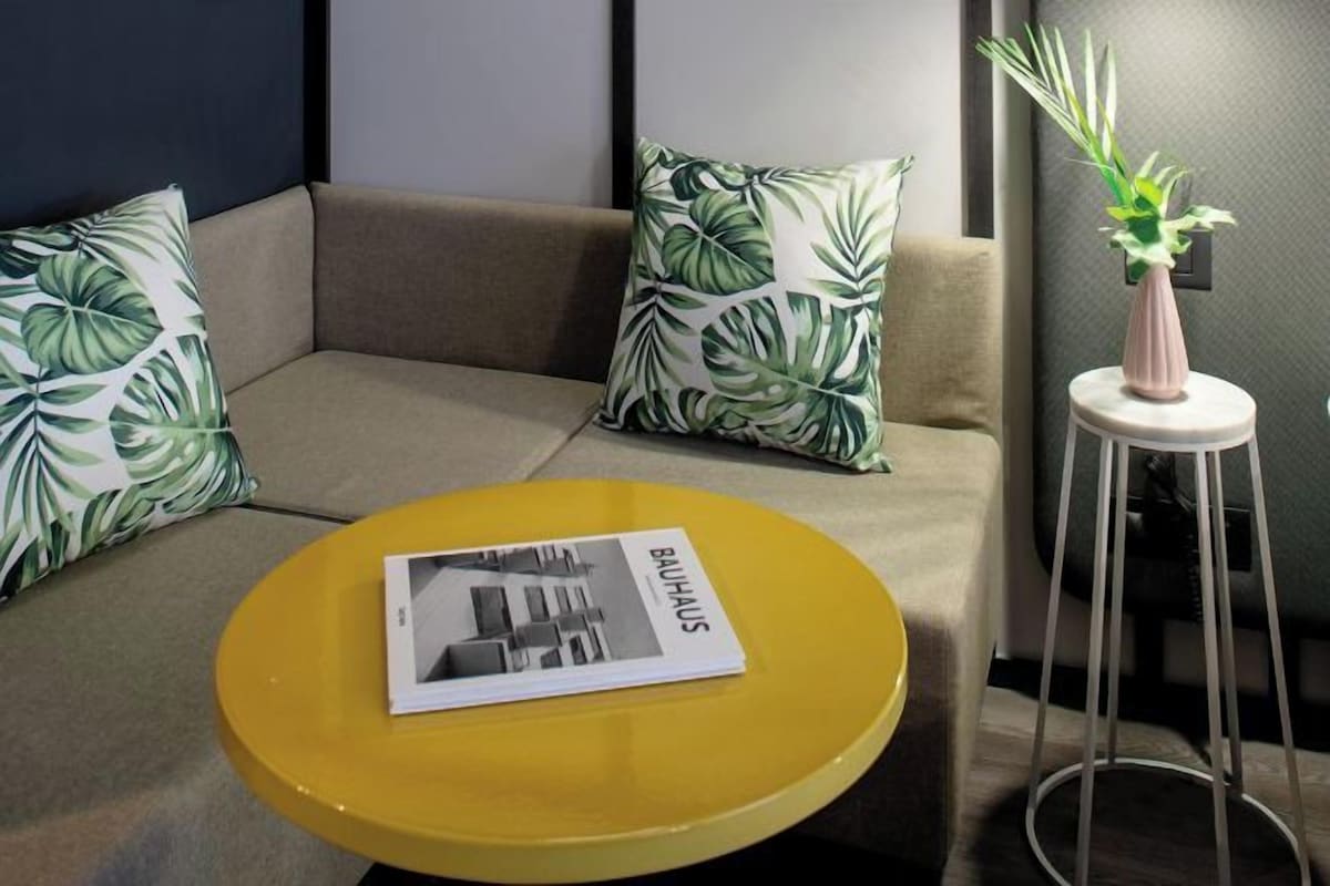 A modern living area with a sofa, a yellow side table, and a potted plant.