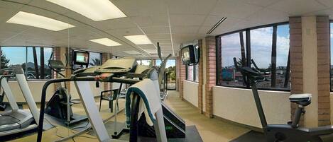 A gym with treadmills, elliptical machines, and a TV screen.