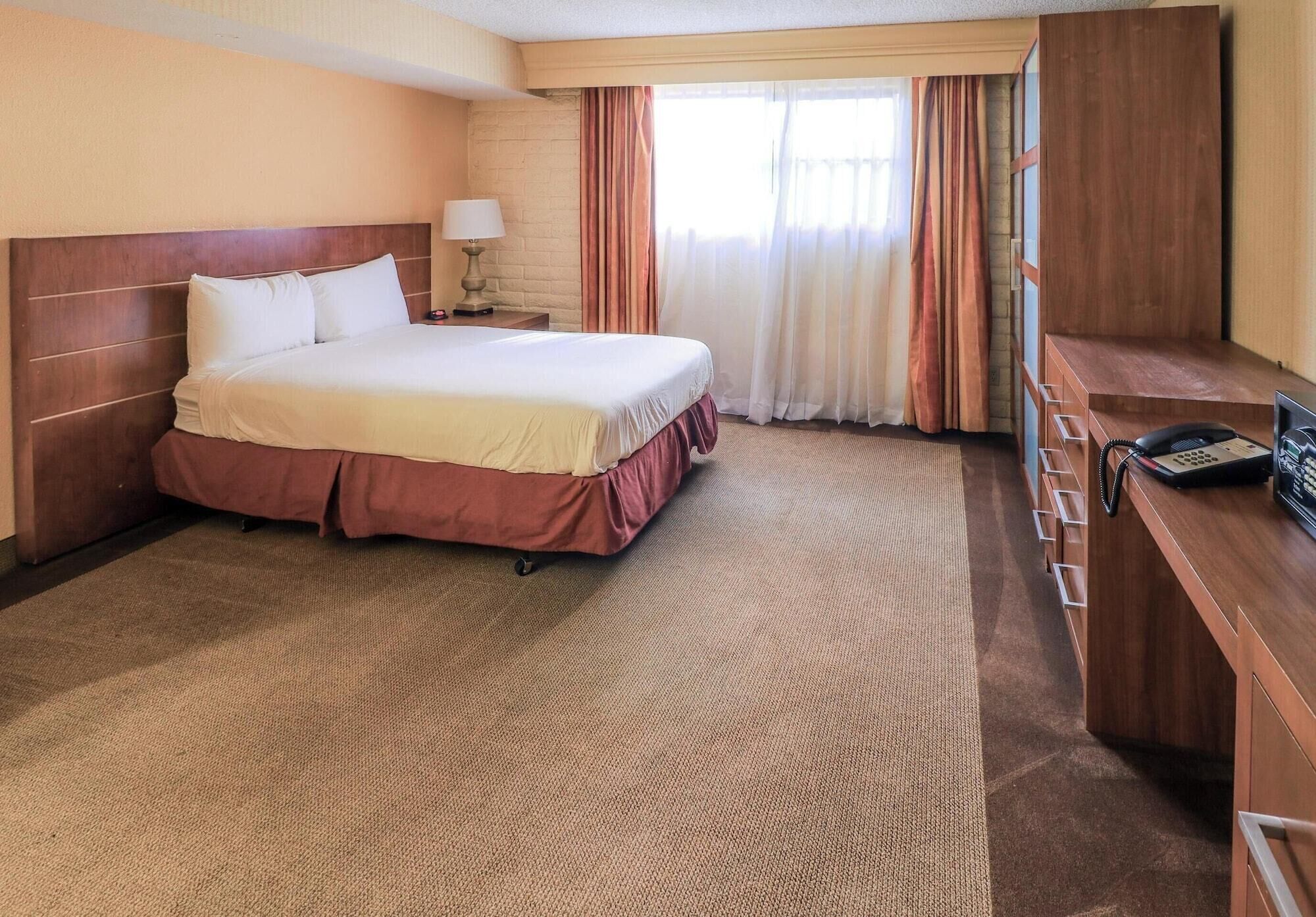 A hotel room with a large bed, a desk with a telephone, and a window with curtains.