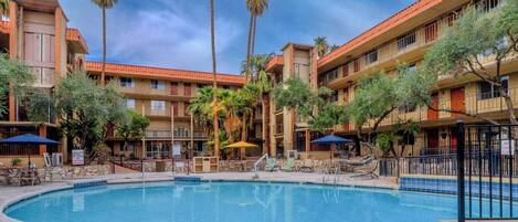 A hotel with a central swimming pool, multiple balconies, and palm trees.