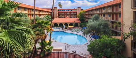 A hotel with a swimming pool surrounded by palm trees and a red-roofed building.