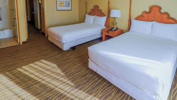 A hotel room with two beds, a wooden headboard, a nightstand with a lamp, and a carpeted floor.