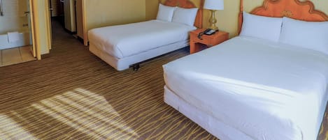 A hotel room with two beds, a wooden headboard, a nightstand with a lamp, and a carpeted floor.