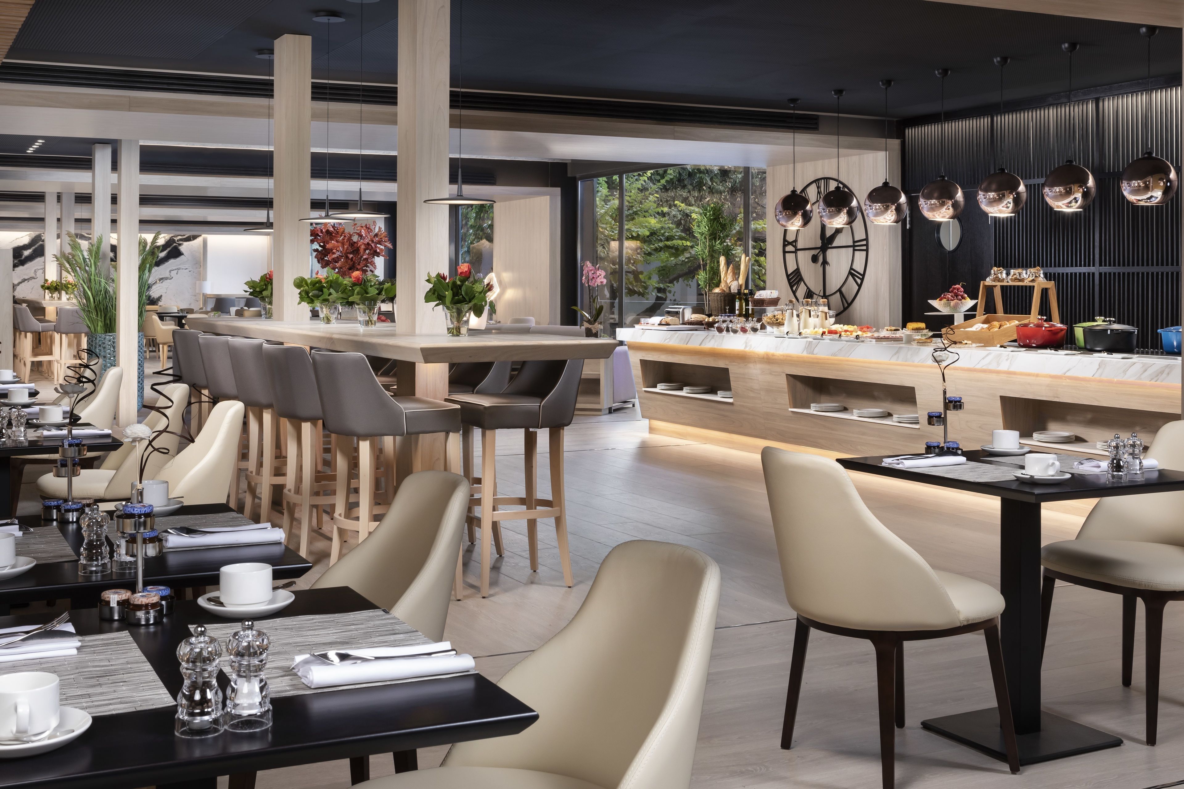 Un ristorante moderno con zona bar, soffitti alti e ampie finestre che offrono vista sull'esterno.