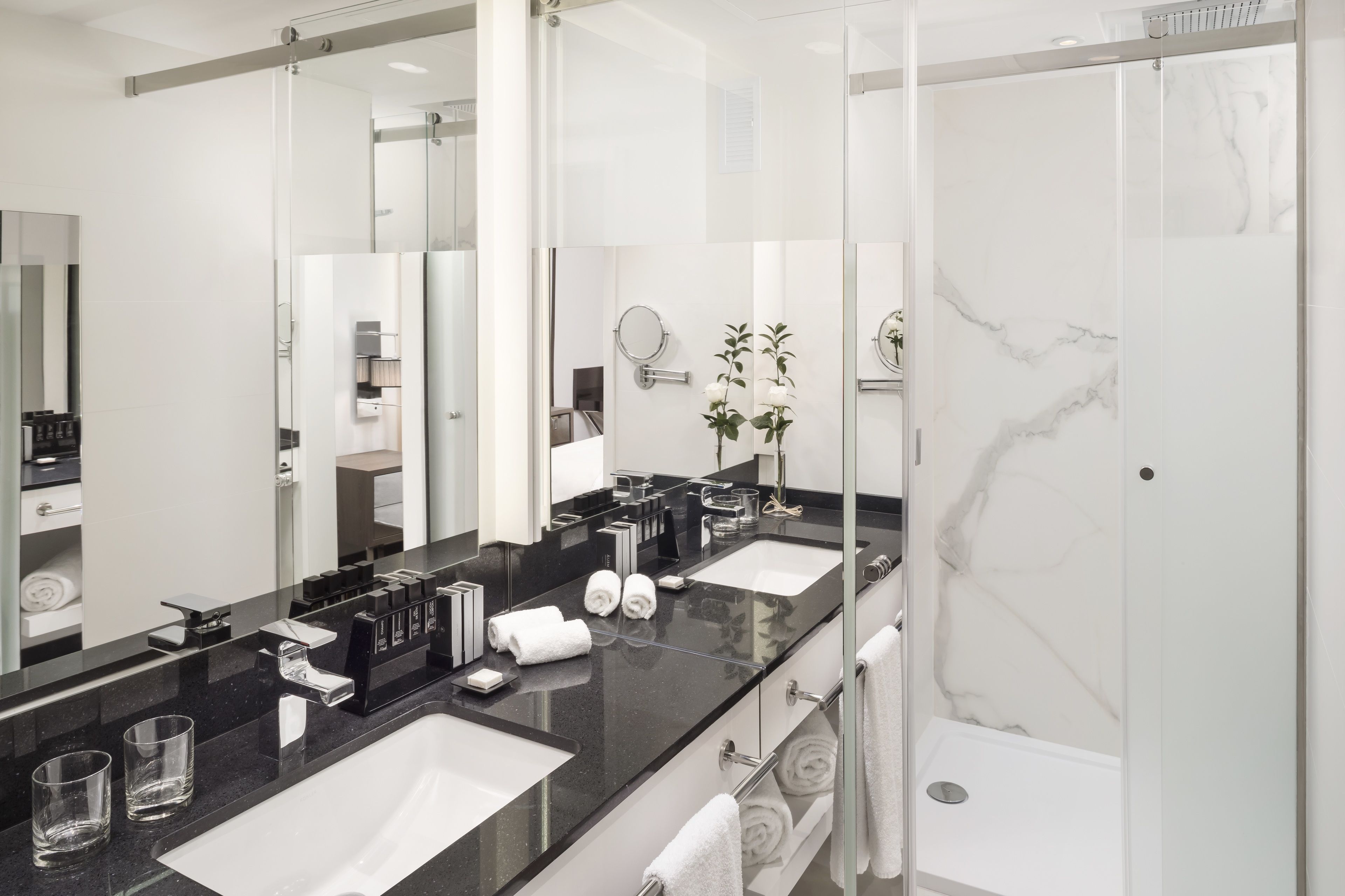 A modern bathroom with two sinks, a large mirror, and a glass shower enclosure.