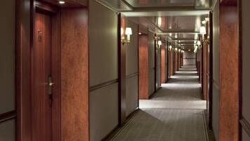 A hotel corridor with wooden doors, a carpeted floor, and wall-mounted lamps.
