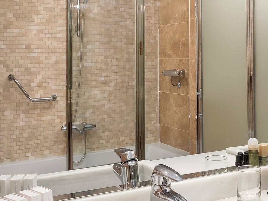 Un baño moderno con ducha de vidrio, un espejo grande y un lavabo blanco con grifería cromada.