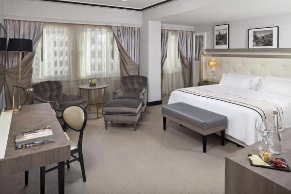 A hotel room with a large bed, two armchairs, a small table, and a desk with a lamp. - Melia Castilla (Madrid)