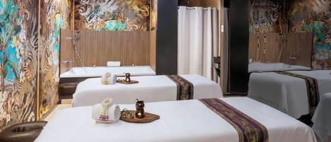 A hotel room with two beds, each with a white bedspread and a decorative headboard. The room features a large, ornate mural on the walls and a wooden panel design on the ceiling.
