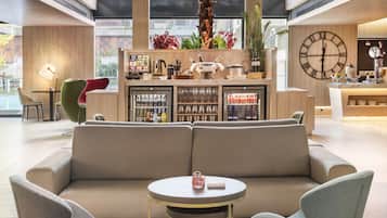 A modern lobby with a sofa, chairs, a small table, a bar area with a clock, and a large window with a view of the outside.