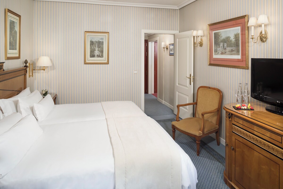 A hotel room with a large bed, a TV, a wooden dresser, and a chair.